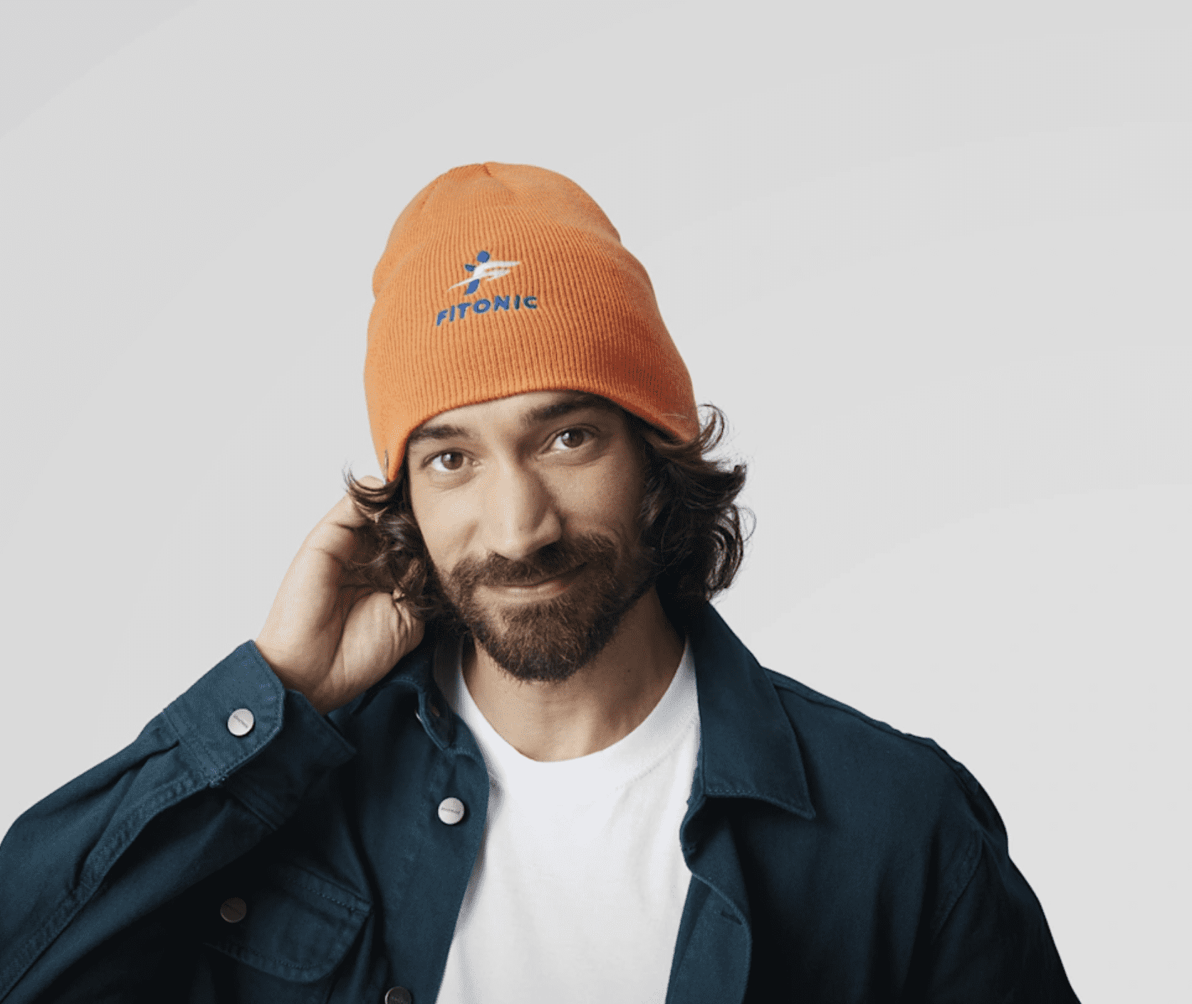 Smiling man wearing orange beanie without cuff and blue-white embroidered logo