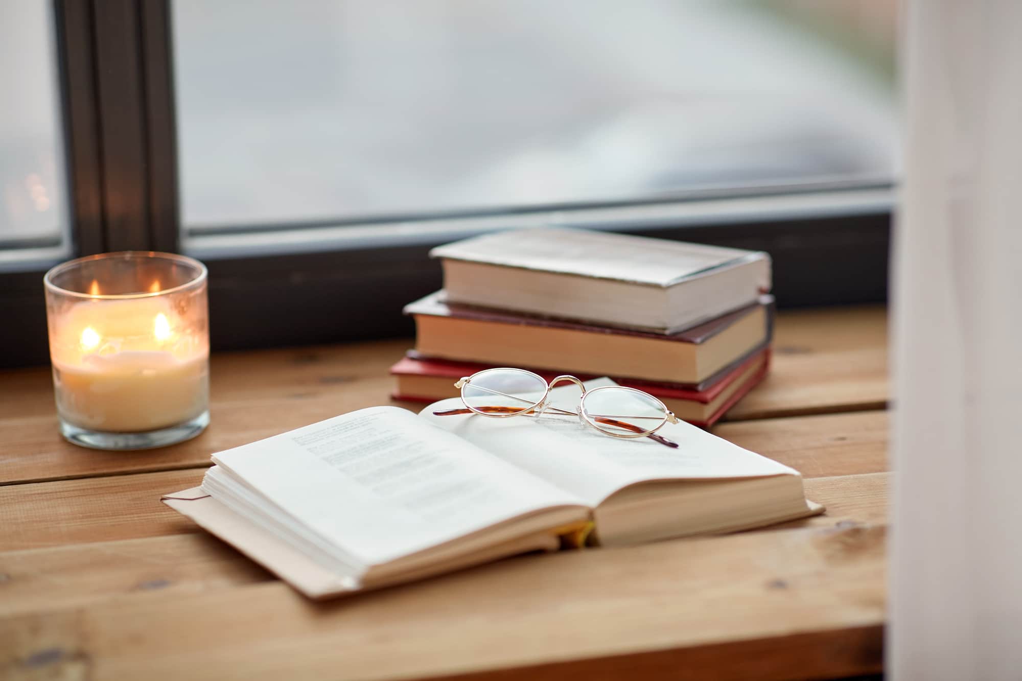 reading, leisure and objects concept - books, glasses and candle burning on window sill
