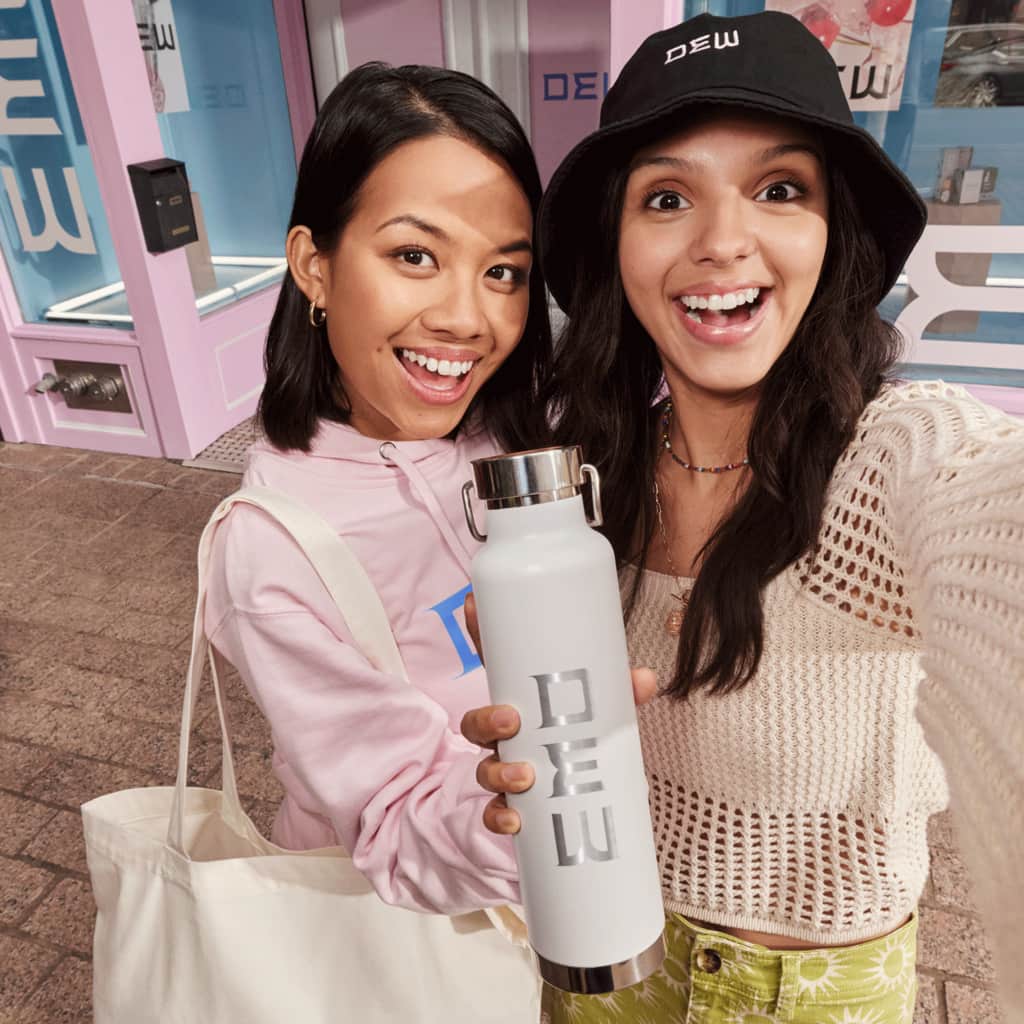 Two women taking a selfie holding up a branded flask outside the store.