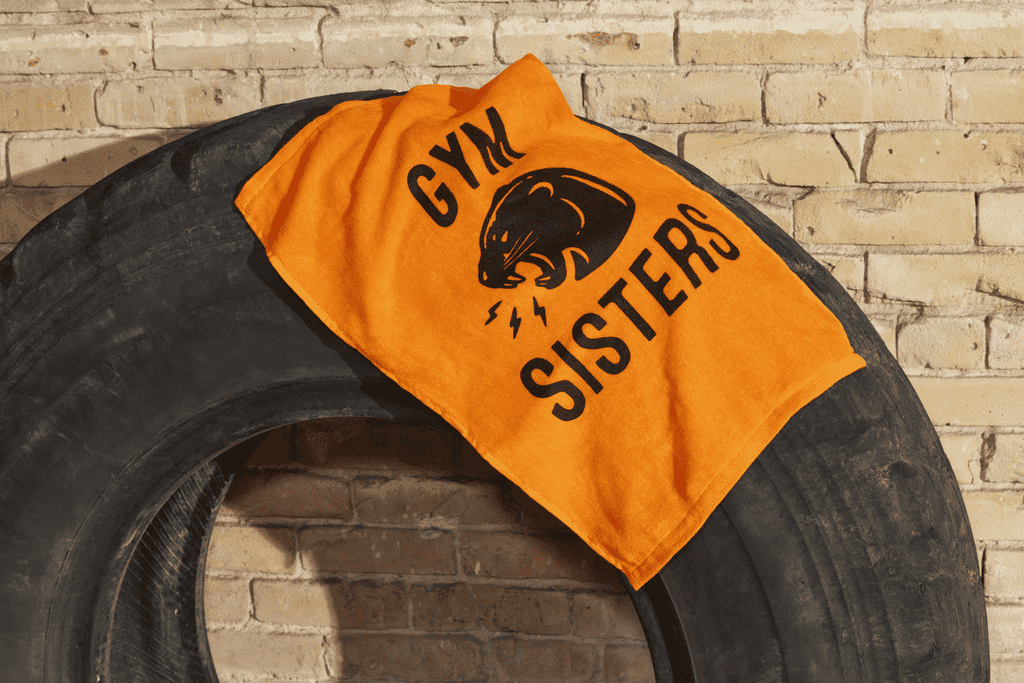 An orange branded sports towel as merch for a gym business on a fitness tire