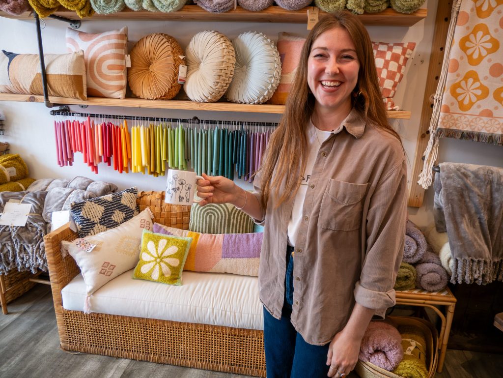 Small business owner of WildFlora standing in her store with a custom mug.