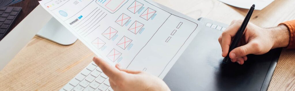 Hand sketches wireframes on table while looking at printed copy
