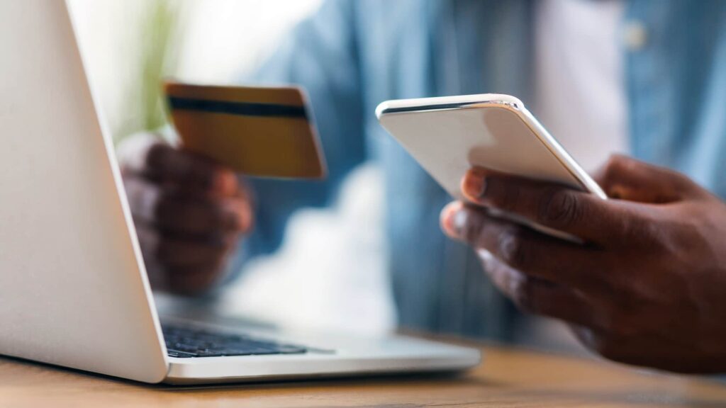 Person holds a credit card and phone in front of an open laptop.