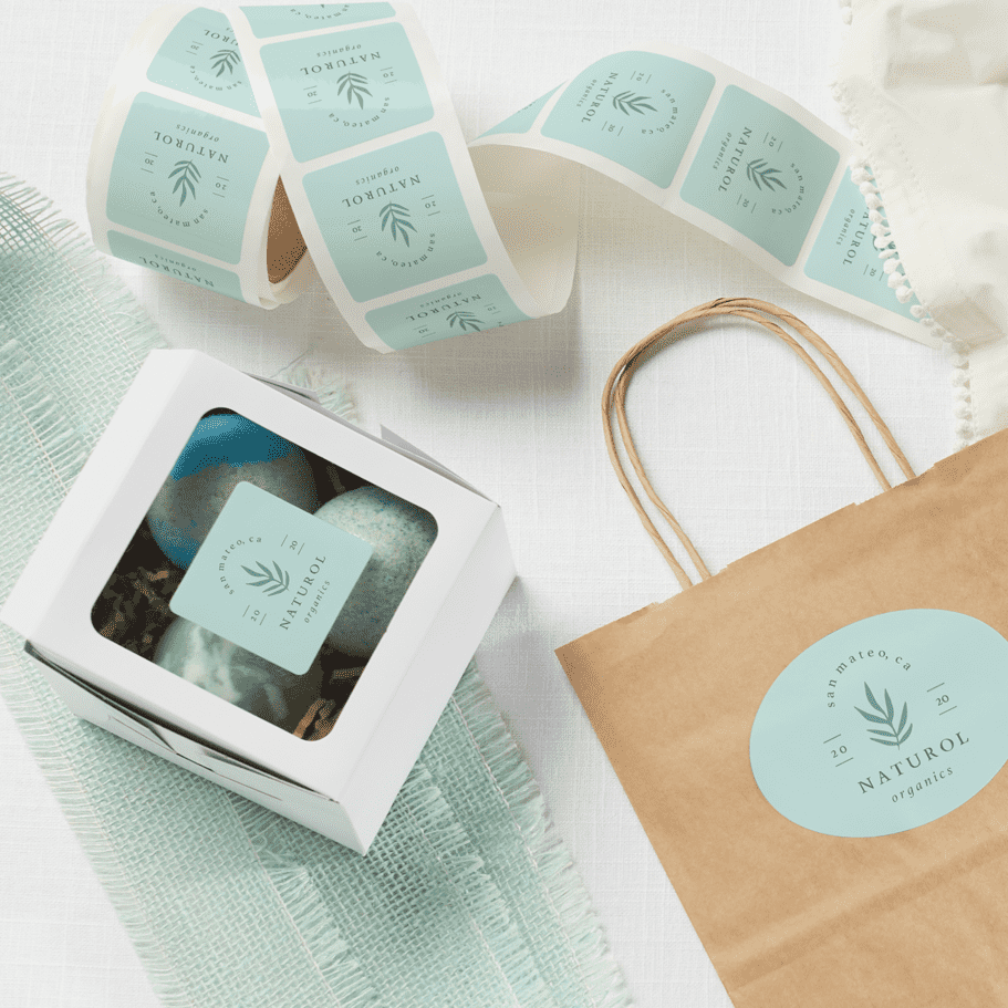 A roll of a small business&rsquo;s custom stickers in light blue, laid across a table with product boxes and kraft paper bags around