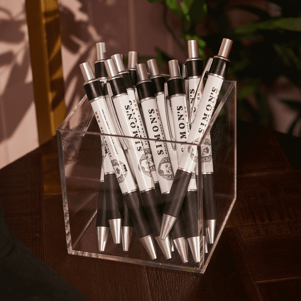 Black an white custom pens with brand name and logo in a clear plastic pen holder resting on a wooden table