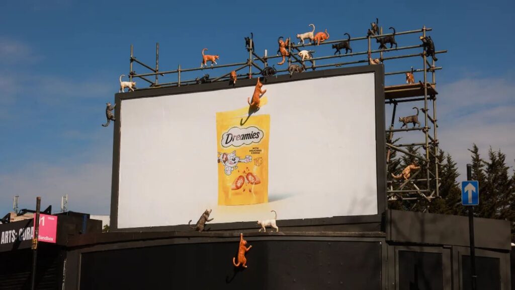 A photo of a DREAMIES OOH billboard surrounded by giant fiberglass cats of all colors&mdash;an example of the Mischief Marketing top marketing trend 2026