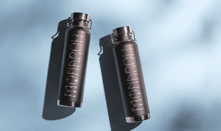 Two sleek, matte black metal water bottles with glossy branding laying on a teal background.
