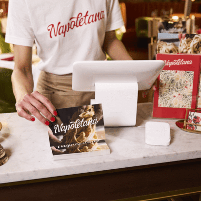 Restaurant host holding a branded postcard at a marble counter, surrounded by menus, business cards and cohesive branding design elements