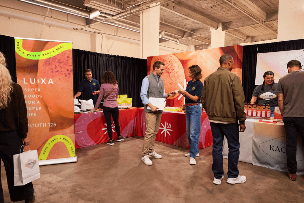 People interacting at branded booths during a trade show, showcasing event marketing materials like banners, table covers and promotional displays