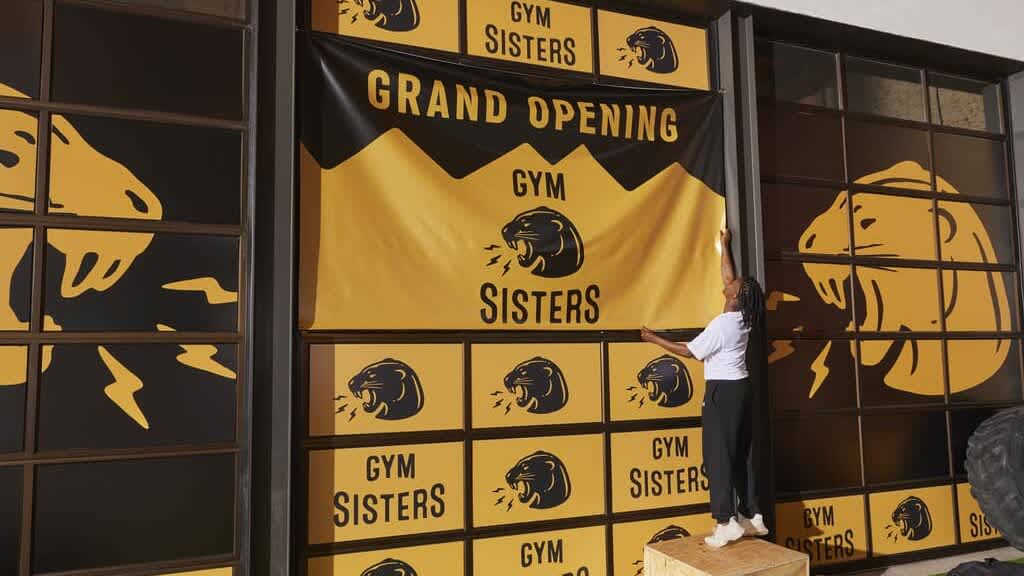 small business owner hanging a branded yellow banner in gym for a grand opening