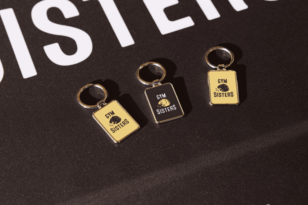 Three branded keychains with the brand logo printed onto the plastic and metallic surface of the merch product