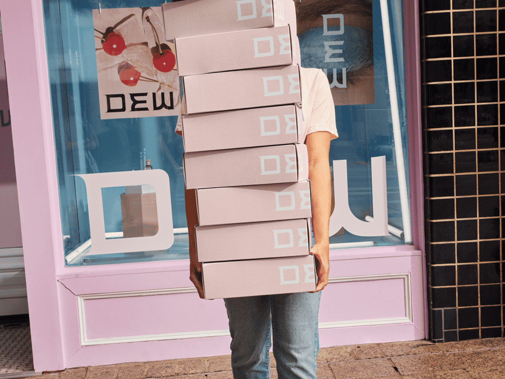 Small business owner holding stack of simple pink custom packaged outside shop, obscuring their face