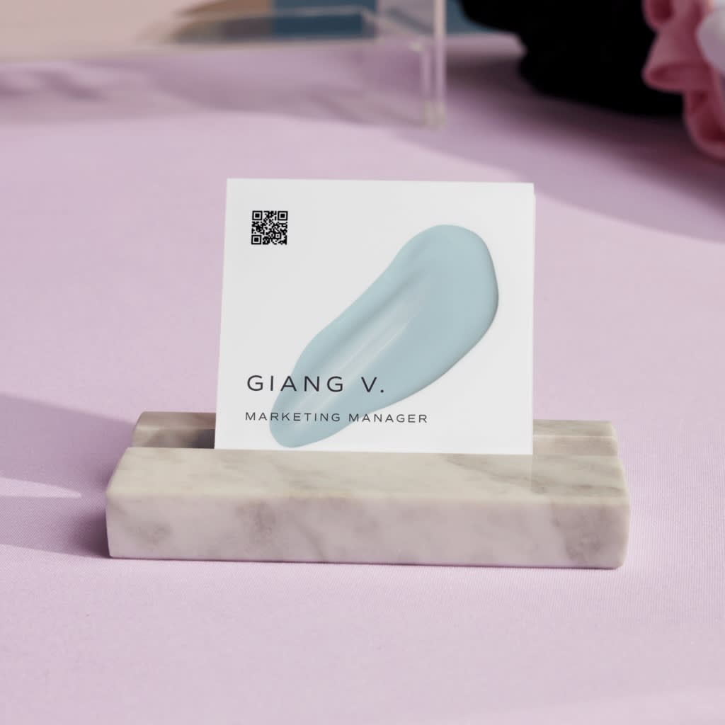 White square business card with smear of light blue paint graphic and thin black contact info text and small black QR code in the corner.