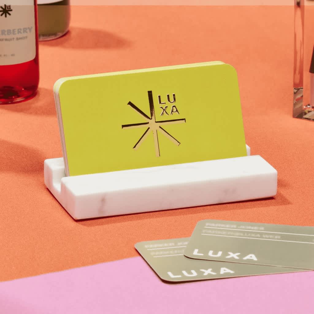 Stack of lime green rounded edge business cards with gold raised foil star logo with “Luxa” text.