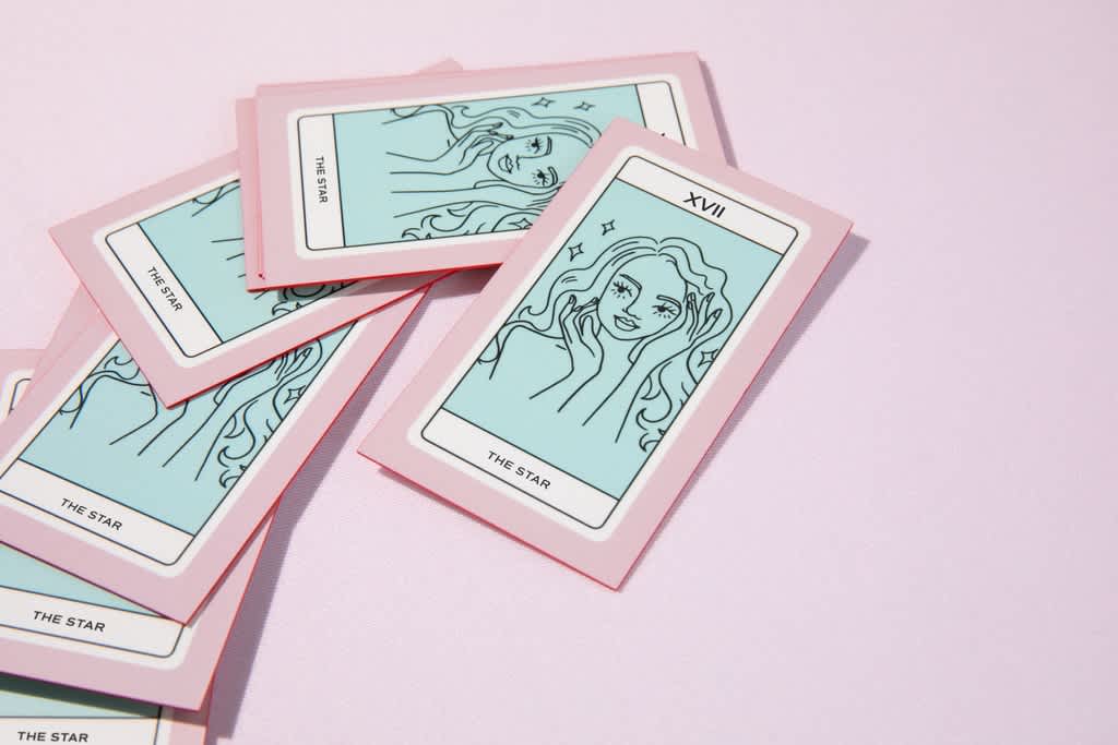 Stack of pink business cards with a light blue and black line drawing tarot style image of a woman with black text “The Star”.